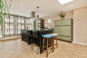 a kitchen and dining area in an apartment with wood flooring, light green cabinets and black bar stools